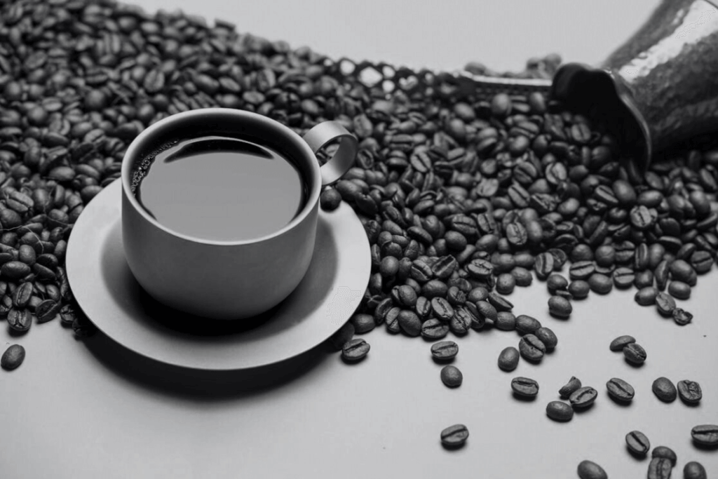 Kaffets ursprung & Historia Kaffekopp som står på bord med utspillda kaffebönor.