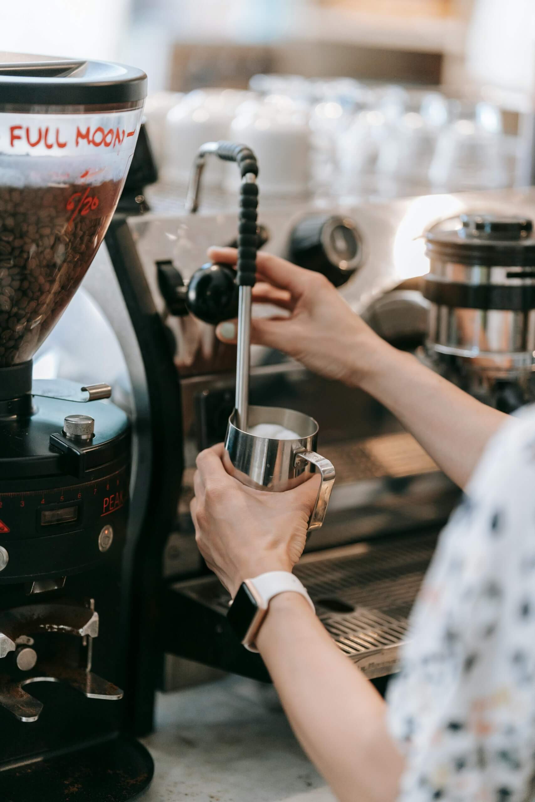 Mjölk skummas på ett café med hjälp av en ångstav på en espressomaskin. Man ser en kvinnas armar som håller i mjölkanna och utför arbetet.