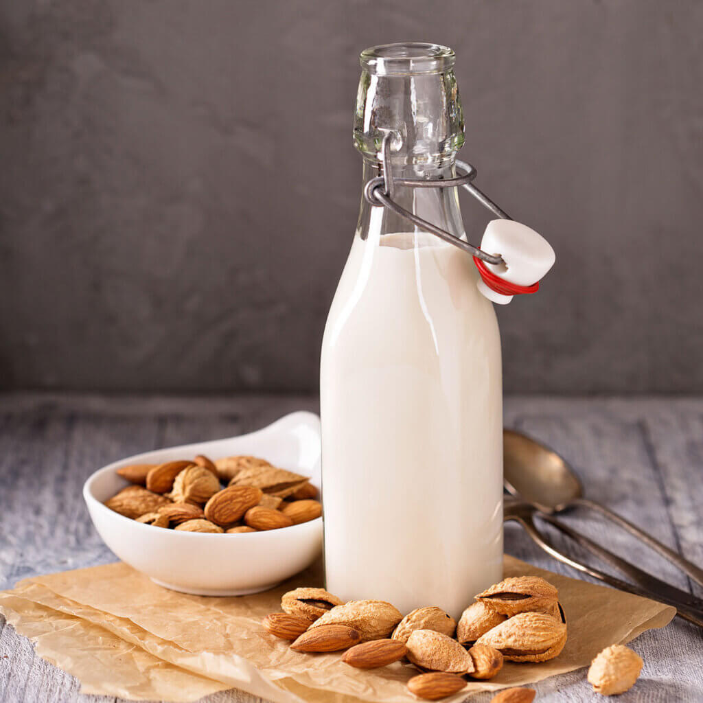 En glasflaska med mandelmjölk. Bredvid står en liten skål med mandlar.