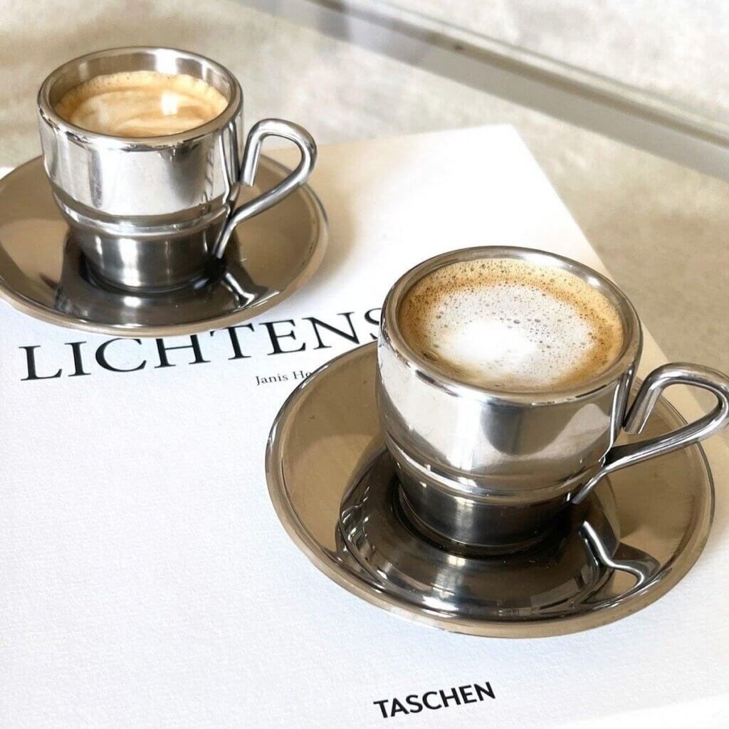 En bild på två kaffekoppar i rostfritt sål som står på en coffe table book.