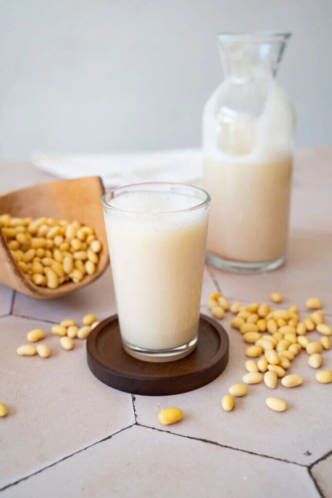 Ett glas med sojamjölk med sojabönor runt om.
